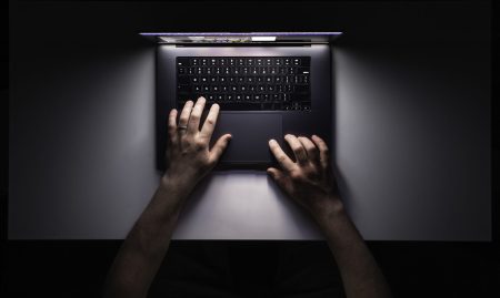 Man using laptop at night, workplace, top view. Minimalistic workplace, working with computer, using laptop at night and online privacy concept.